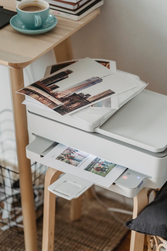 Home A cozy home office corner with a printer, coffee cup, and printed photos on a wooden table.